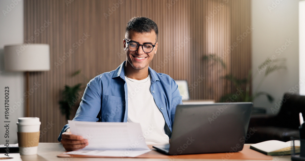 Fototapeta premium Man, smile and document in home with laptop, remote work and proposal for digital marketing campaign. Person, paperwork and computer in house with idea, creativity and plan for freelance advertising.