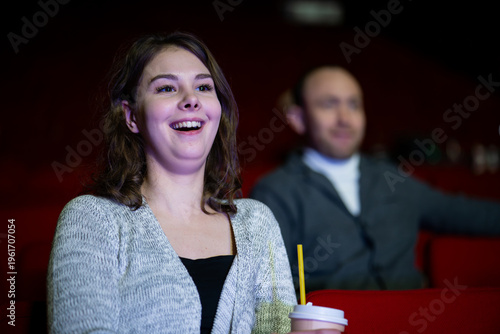 Fotografi smiling woman with popcorn watches a movie in a cinema, enjoying a comedy or humorous film