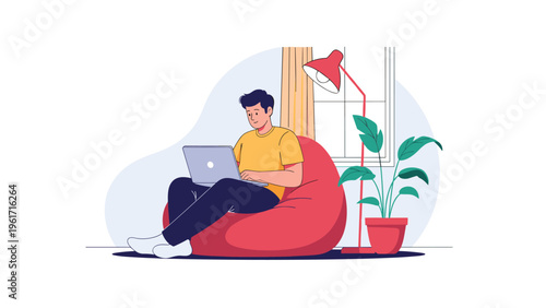Focused young man works remotely on his laptop while sitting comfortably in a red beanbag chair at home with a lamp and plant.