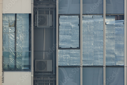 Grimy glass windows of an abandoned condominium, covered with crumpled aluminum foil for sun blocking, symbolizing a real estate crisis or housing bubble.
