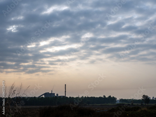 Factories and tall smokestacks stand alone amidst agricultural and wasteland areas