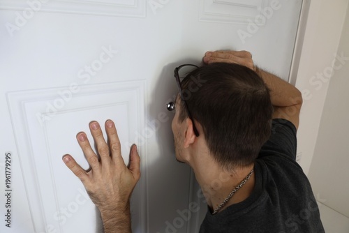 Close-up of a man pressing his face to a door peephole to look outside. Concept of curiosity, fear, and home security.