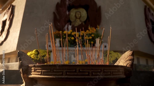 Incense sticks burning at a temple with flowers in the background during a sunny day