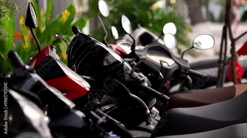 Motorcycles lined up in a parking area during daytime at a tropical location near plants