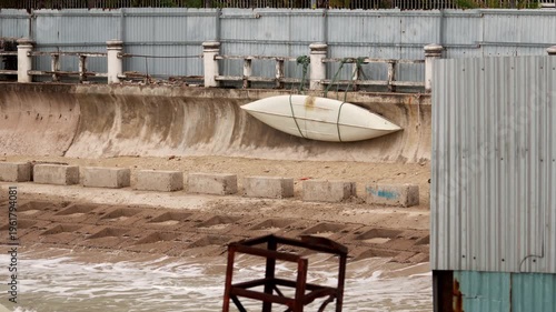 Kayak resting on a wall near water with a concrete shoreline and metal structure in the foreground during cloudy weather