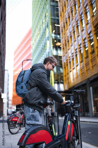 Canvas Print Young man standing on a london city street, connecting his smartphone to an elec