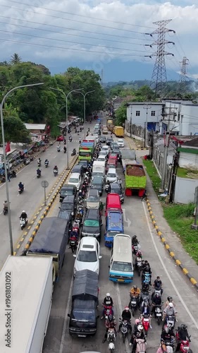 Severe traffic jam on a busy urban road with dense motorcycles and vehicles, bordered by trees and buildings under a cloudy sky