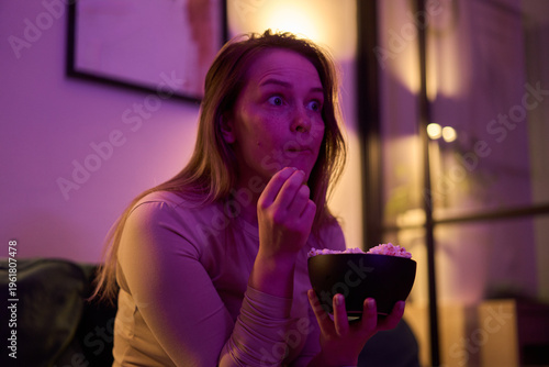 Female holding popcorn bowl while watching screen indoors