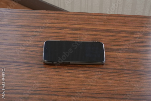 Black smartphone rests on polished wooden surface. Simple, clean composition draws attention to device. Ideal for tech, product, or minimalist design projects