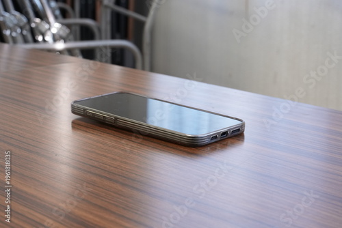 Modern smartphone rests on polished wooden table. Minimalist scene suggests calm, focused environment. Clean lines and soft lighting enhance tech appeal. Ideal for business, lifestyle