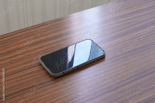 Smartphone rests on a warm, wooden surface. Reflective screen mirrors the room's soft light. Minimalist setup suggests calm, focused use. Ideal for tech, lifestyle, or minimalist design projects