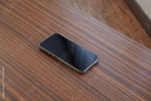 Smartphone rests on rich wood grain surface. Minimalist composition, clean and modern. Device reflects ambient light softly. Ideal for tech, lifestyle, or product showcase