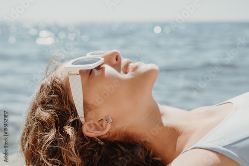 Woman, sunglasses, ocean. Young woman relaxing by the sparkling ocean, enjoying a peaceful summer vacation with copy space.