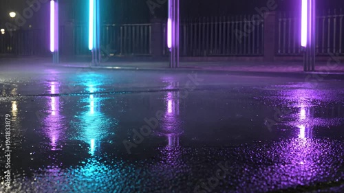 Rain falling on a wet asphalt street at night with glowing blue and purple neon lights. Seamless loooing 4k video background