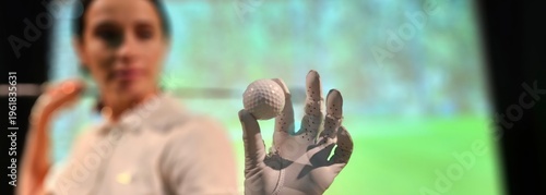 A golfer prepares to swing, holding a golf ball in an indoor training facility