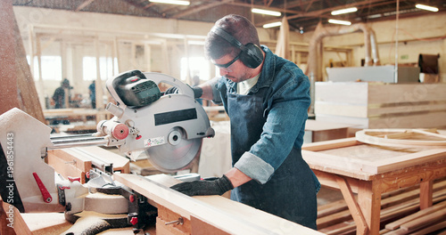 Fotografie Man, carpenter and miter saw for wood at warehouse with manufacturing process at industrial plant