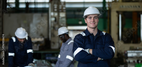 Industrial engineer standing with arms crossed in factory, confident professional worker leading manufacturing team, engineering leadership and workforce productivity in industrial operations.