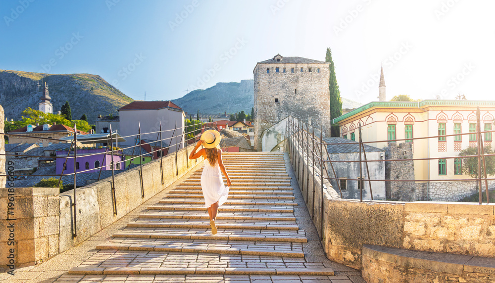 Fototapeta premium Woman in white dress walking on Stari Most bridge, sunset over old town Mostar, Bosnia and Herzegovina
