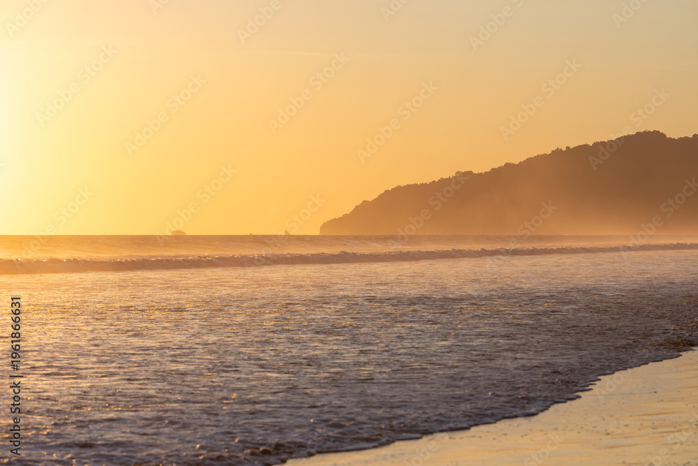 Obraz premium The low sun's golden light illuminates the ocean spray on Carate Beach, with views of Corcovado NP at sunset. Costa Rica.