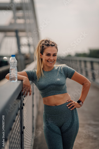 Sporty woman drinking water after training on the bridge