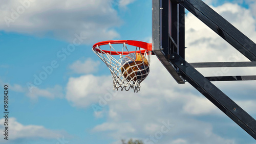 Photos Basketball going through hoop net against a blue cloudy sky