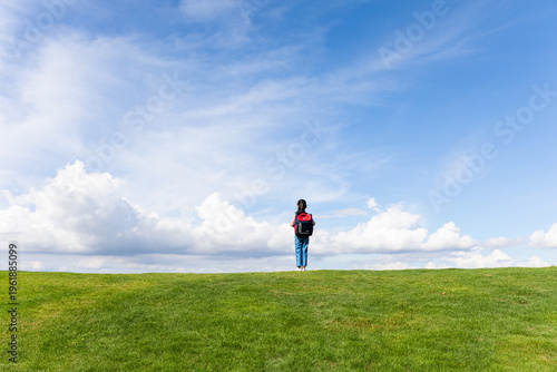 A little Chinese girl carrying a school backpack on the blue sky grassland