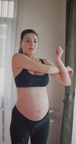 Pregnant woman stretching her arms and shoulders at home.