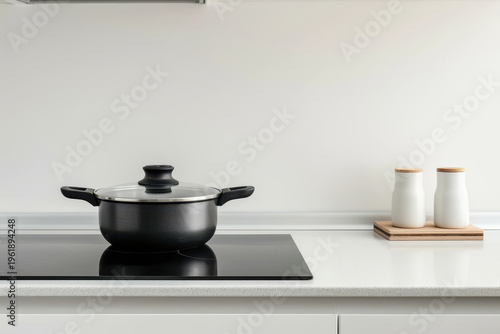 Black cooking pot sitting on an induction hob on a white countertop in a minimalist kitchen