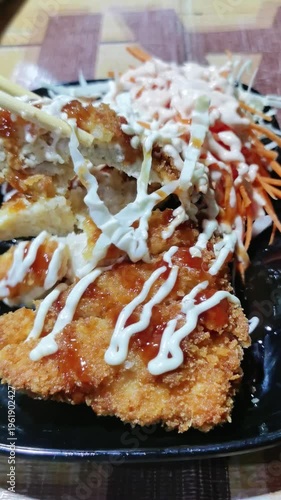 Crispy breaded chicken cutlets drizzled with sauces served with fresh vegetables on dark plate