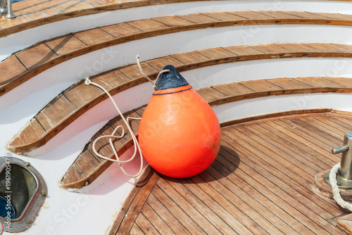 Orange inflatable marine fender on wooden steps of a luxury yacht deck near the water and mooring equipment