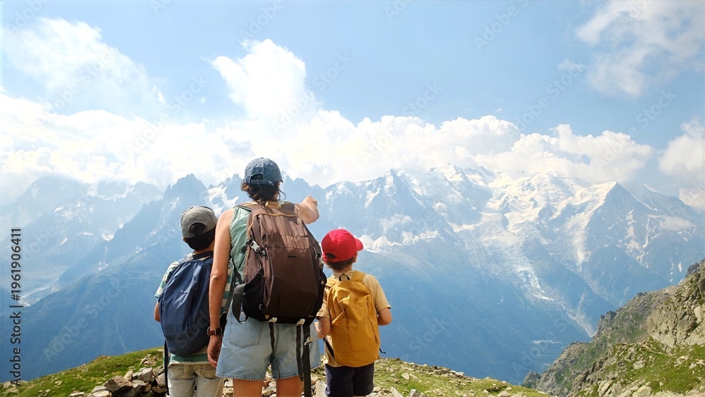Naklejka premium Family enjoying mountain hiking, woman pointing towards the vast snowy alps peaks, children exploring nature during a summer adventure trip with scenic views