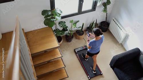 фотографія Woman using a smart treadmill for an indoor workout at home, checking fitness da