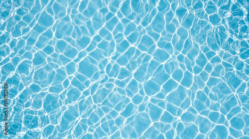 Abstract overhead blue swimming pool water texture with bright white caustic light ripple patterns creating geometric mosaic-like network across turquoise surface.