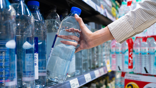 Fotografie Close-up of a shopper's hand grabbing a clear plastic water bottle from a supermarket shelf