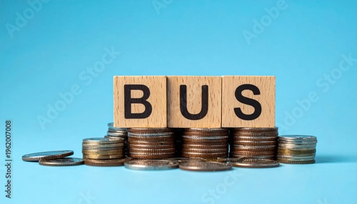 Conceptual image of business success and financial growth represented by stacked coins and wooden blocks spelling BUS on a vibrant blue background with soft lighting