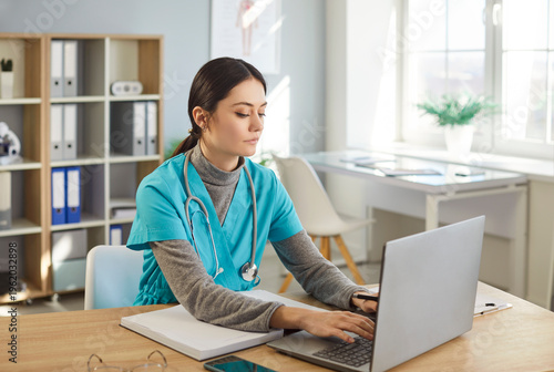 Focused woman, doctor or nurse, working online with laptop in clinic office, conducting research and preparing prescription, healthcare commitment in a structured medical space of investigation.
