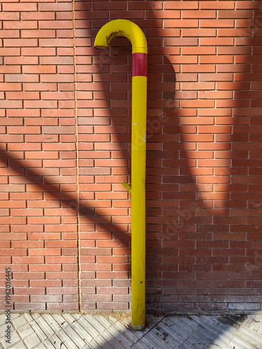 Bild auf Leinwand Yellow natural gas pipeline vent pipe for cathodic protection and ventilation installed against a red brick wall on a city sidewalk