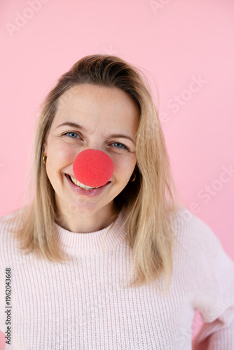 blond woman in front of pink background with red clown nose