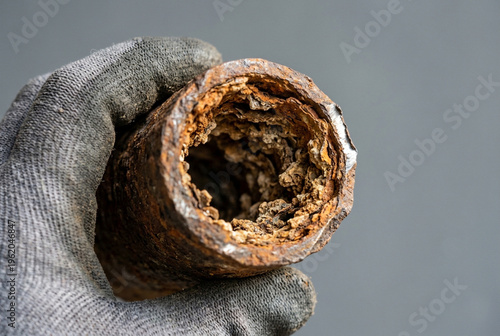 Close-up of a clogged plastic drain pipe held by a gloved hand, with a finger pointing to heavy buildup inside. Concept of blocked drain, limescale/grease deposits, plumbing problem, home maintenance