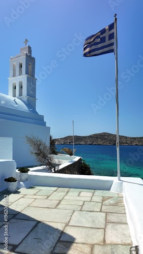 View of the beautiful whitewashed church of Agia Irini next to the Greek national flag
