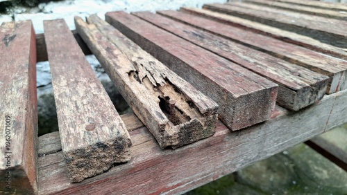 Rusty nail embedded in rotten wood surface of an old abandoned garden bench with rough rustic texture and brown weathered wooden plank background