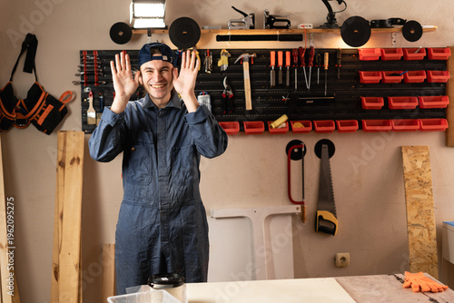 Фотография funny carpenter man with diy tools for maintenance and repair work making faces at camera, fooling around and joking in workshop