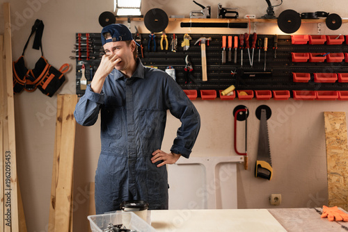 Carpenter man with diy tools for maintenance and repair work closing his nose repulsed by unpleasant odor in workshop. Woodworking and carpentry. Terrible smell