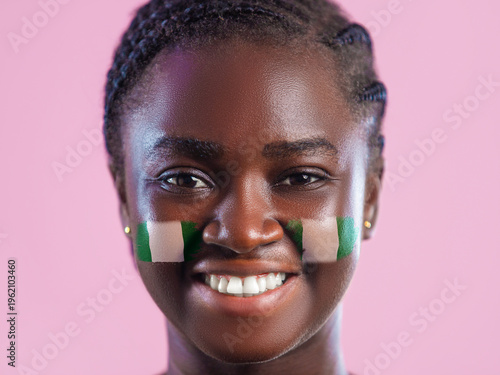 Foto A smiling young Black woman with braided hair has the Nigerian flag painted on her cheeks
