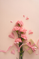 Happy Mother's Day vertical arrangement of pink carnations with ribboned gift and paper hearts on a soft pastel background evoking tenderness and appreciation