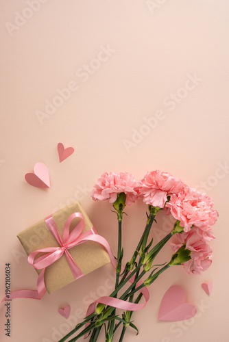 Happy Mother's Day vertical concept with pink carnations, a wrapped gift tied with satin ribbon, paper heart cutouts and soft pastel background evoking love, appreciation and gentle feminine style