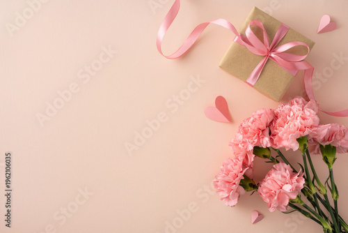 Happy Mother's Day concept featuring pink carnations, a wrapped gift with satin ribbon and paper hearts on a soft peach background ideal for cards and social media visuals