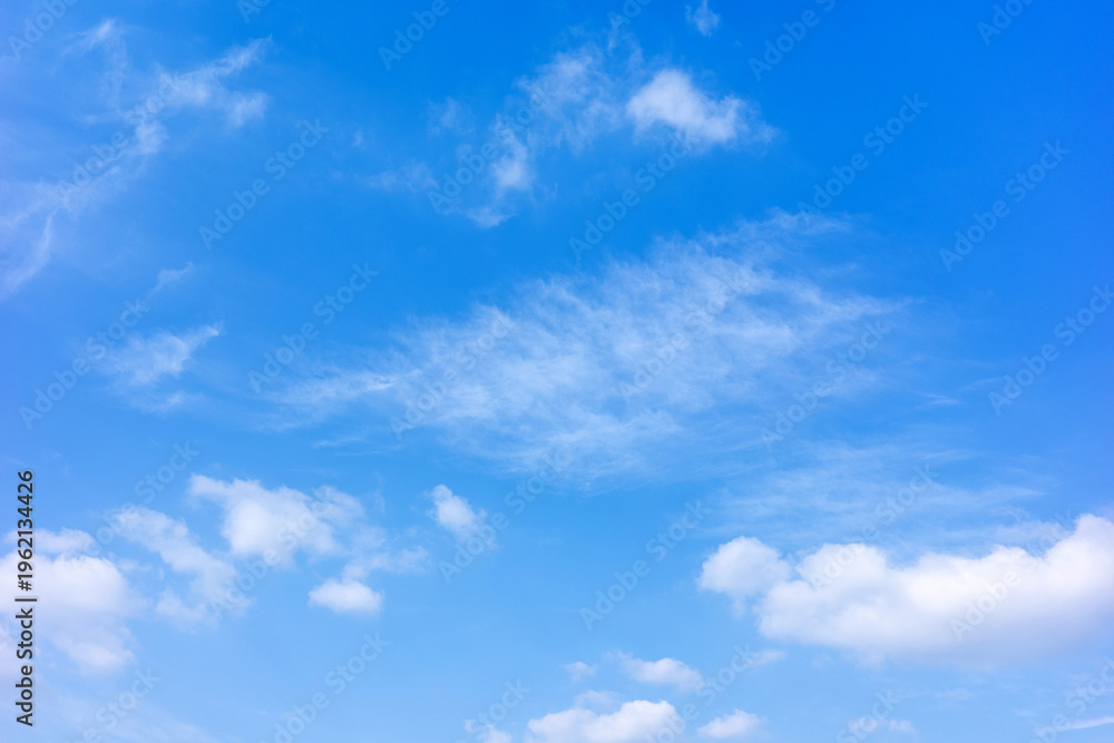 Fototapeta premium This bright, horizontal shot captures a breathtakingly clear blue sky adorned with soft, wispy cirrus clouds and scattered white cumulus formations during a sunny day.