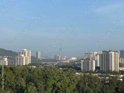 Photography Modern residential apartment buildings standing among green trees with distant Kuala Lumpur city skyline and mountains under blue sky