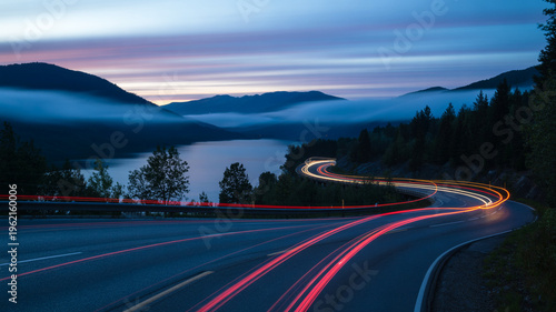 Winding road with light trails at dusk near lake and mountains